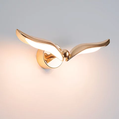 Sur un fond blanc on voit une application murale en forme d'oiseau dorée allumée.