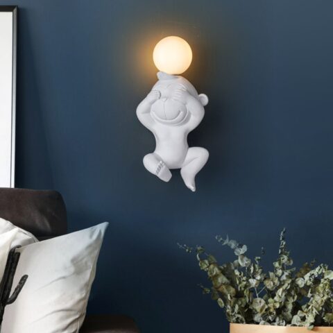 Sur un mur bleu foncé on voit au milieu accrochée, une applique murale en forme de singe blanche allumée.