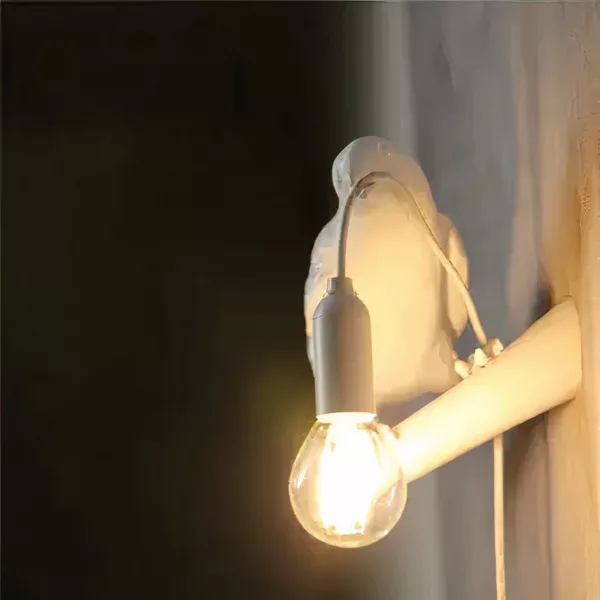 Sur un fond noir on voit une applique murale en forme de corbeau blanche allumée.