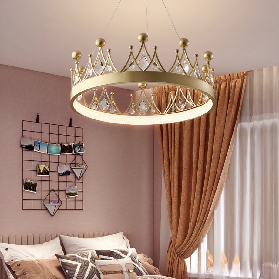Lampadario a forma di corona per la camera del bambino Lampadario pour chambre de bébé en forme de couronne de couleur doré, avec des pierres en cristal sur celle ci, dans une chambre aux murs roses