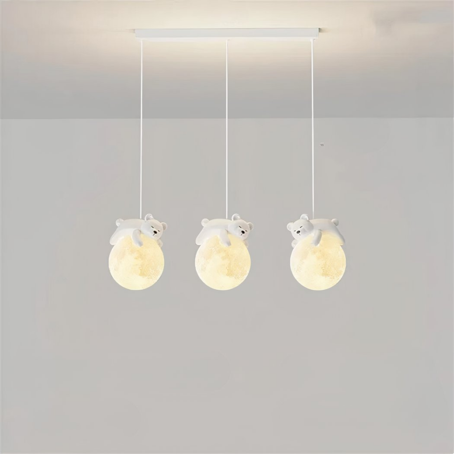 Luminaire suspendus, composé de trois câbles avec chacun une boule qui représente la lune, et un nounours qui dort sur la lune. Les boules sont allumées. Le socle rectangulaire est accroché au plafond gris clair, on voit dans le fond un mur gris clair aussi.