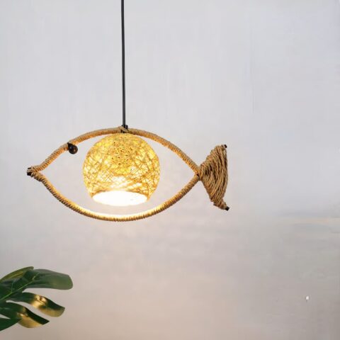 Lampadario en corde enroulée autour d'une tige métallique en forme de poisson, suspendu. Avec une abat-jour au centre en forme de boule. Derrière on voit un mur gris et en bas à gauche on voit un morceau de plante verte.