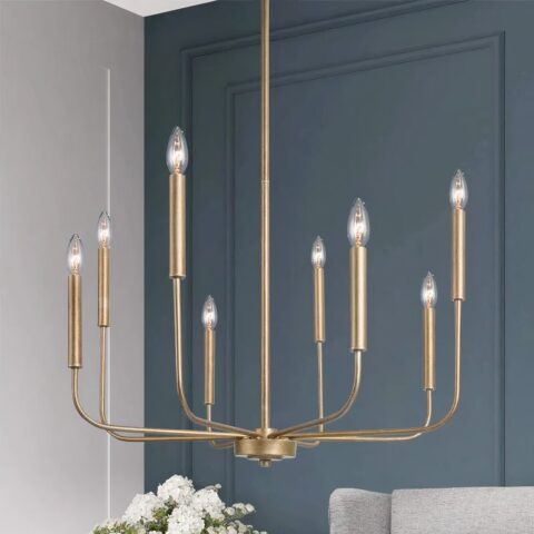 Lampadario en métal doré, en forme de chandelier avec 8 bougies à ampoule. Derrière, au fond, on voit un mur bleu canard, un bout de bouquet de fleurs blanches et un bout de canapé gris clair.