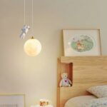 Lampadario de style nordique en résine avec astronaute sur fond beige avec un lit à droite