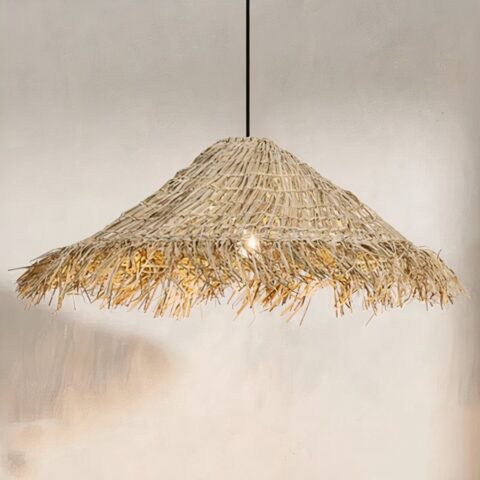 Lampadario en paille suspendu, de forme conique comme un chapeau. En paille tressé, avec les bords en paille brossé. Derrière on voit un mur beige et à droite un bout de l'ombre de l'abat-jour.
