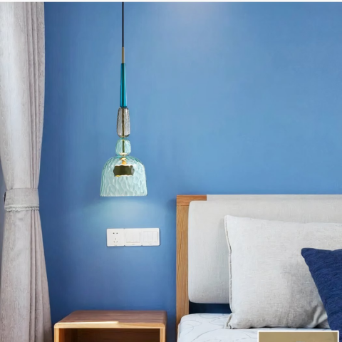 Lampadario suspendu LED moderne en verre coloré sur fond bleu avec un lit à droite