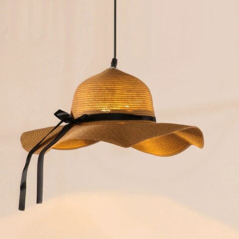 Lampadario original chapeau de paille allumé et suspendu sur fond beige clair.