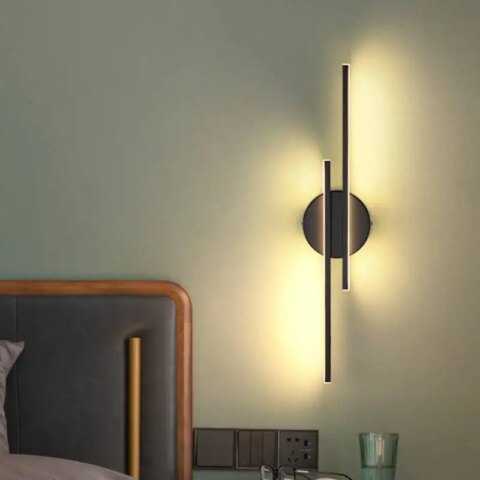 Applique murale linéaire design moderne accrochée sur le mur d'une chambre à coucher et allumée, à côté du lit.