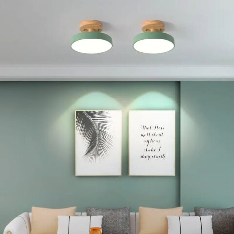 Lampadario plafonnier rond pour chambre en bois et métal installé au plafond et allumé, en version verte, au-dessus d'un canapé.