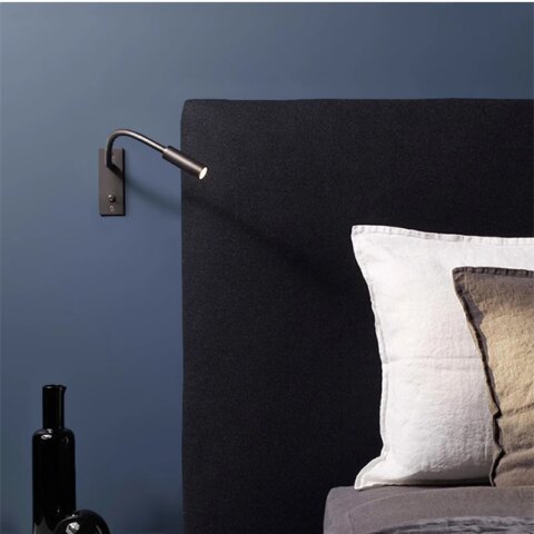 Applique murale liseuse avec interrupteur accrochée à un mur bleu d'une chambre et à côté d'un lit.