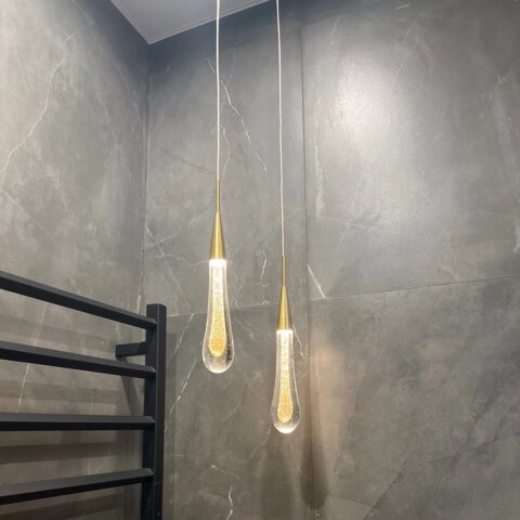 Lampadario en forme de goutte d'eau suspendu au plafond, dans une pièce aux murs gris.