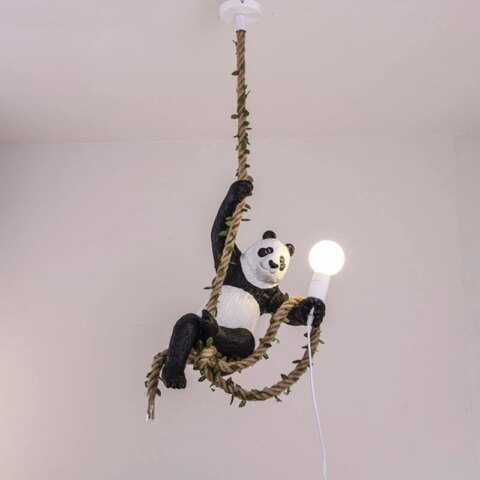 Suspension avec corde en chanvre entrelacée de feuillage. Un panda est accroché par sa patte avant droite, la corde passe dans ses pattes arrières et il tient une ampoule allumée dans sa patte avant gauche avec une partie de la corde.
