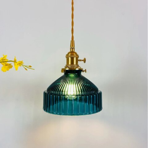 Suspension vintage avec câble torsadé doré et douille dorée, abat-jour bleu canard ressemblant à une cloche avec stries sur tout le tour. Lampadina allumée. Fleurs jaunes à gauche.