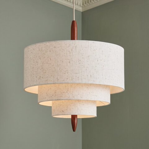 Lampada a sospensione giapponese in tessuto beige con tre paralumi rotondi davanti a una parete verde